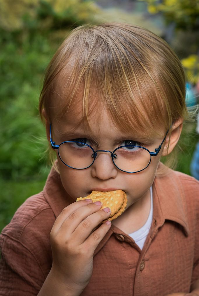 Portraitaufnahme eines Kindes, dass eine blaue Brille trägt und in einen Keks beißt